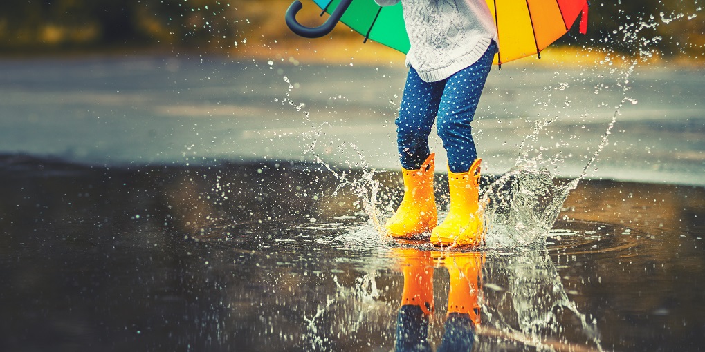 A child splashing in a puddle wearing yellow wellington boots